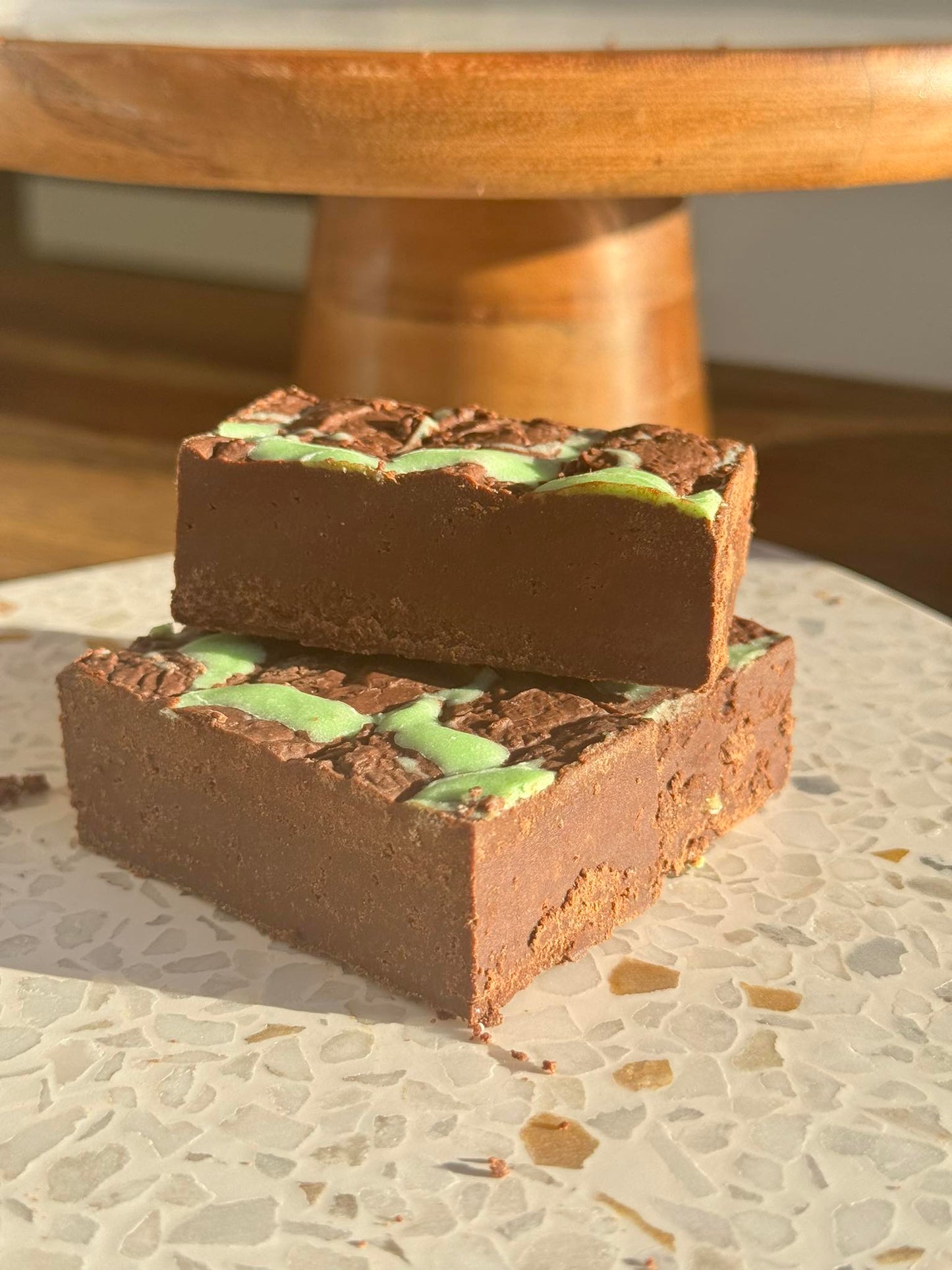 Three Chocolate Keto mint slices are stacked ontop of each other with a wooden board behind them